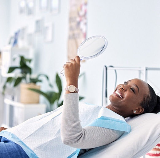 Woman smiling at reflection in handheld mirror