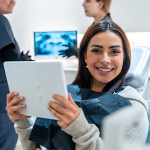 Patient smiling while holding mirror in treatment chair