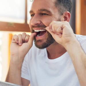 Man smiling while flossing his teeth in bathroom