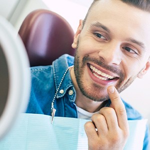 Man smiling at reflection in handheld mirror