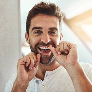 Man smiling while flossing his teeth at home