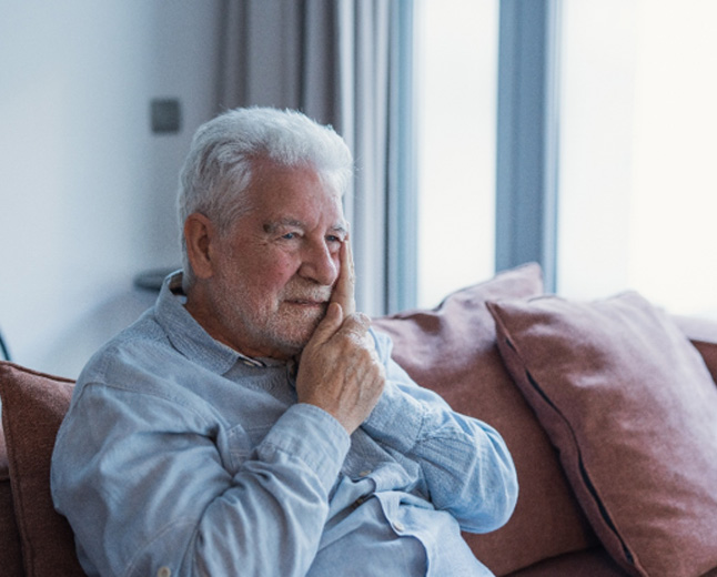 Older man sitting on couch with pain from failed dental implant in Kingman